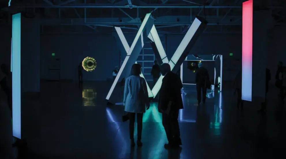 Two people in darkly lit museum room with glowing technology sculptures.