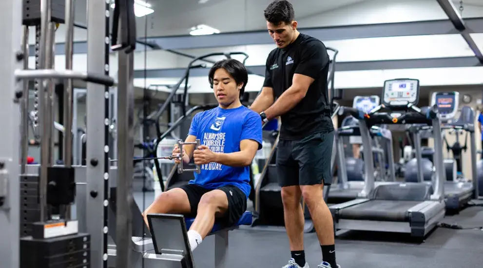 Student exercising in the gym with a personal trainer.