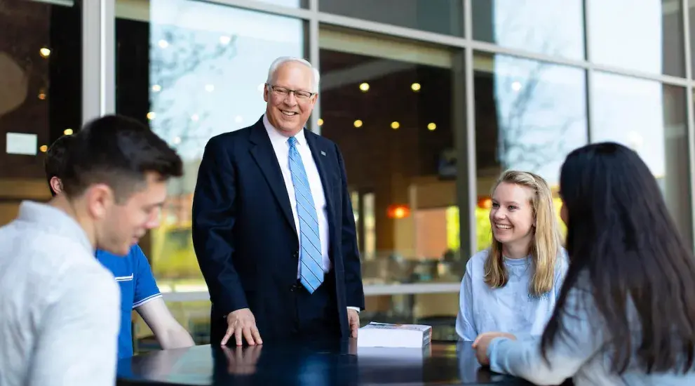 Dean Hendrickson talking with business students at outside table.