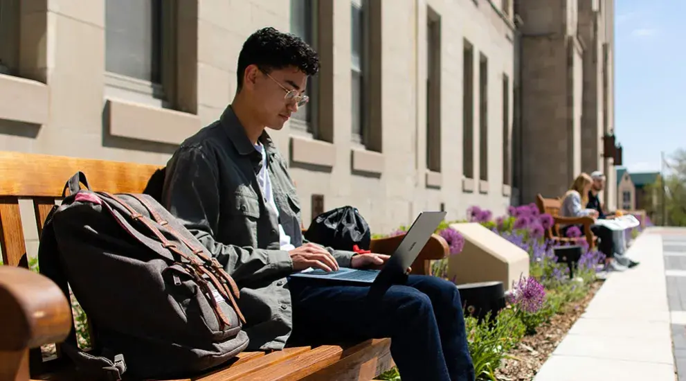Student working on a bench using a laptop