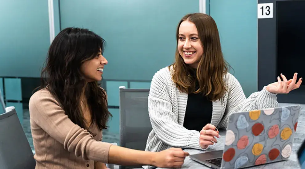 one white female student and one Indian female student talking