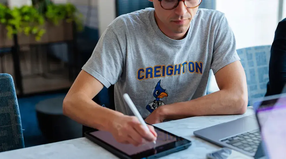 Student working on tablet and laptop at table