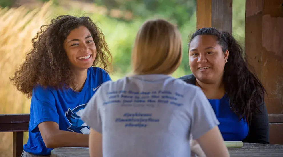 Three students sitting at table outdoors