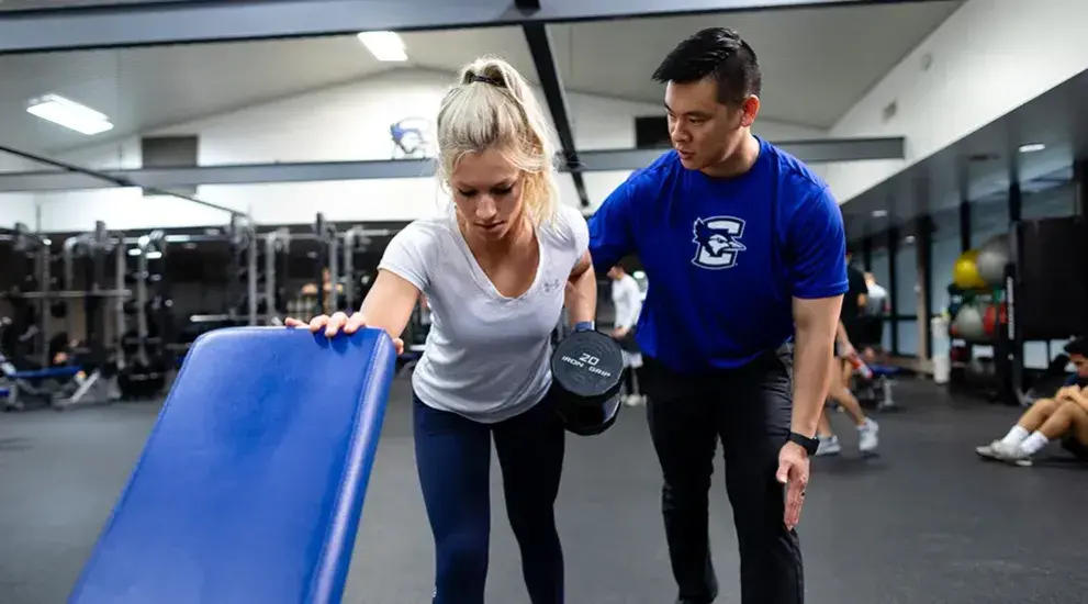 Student working with trainer lifting weights.