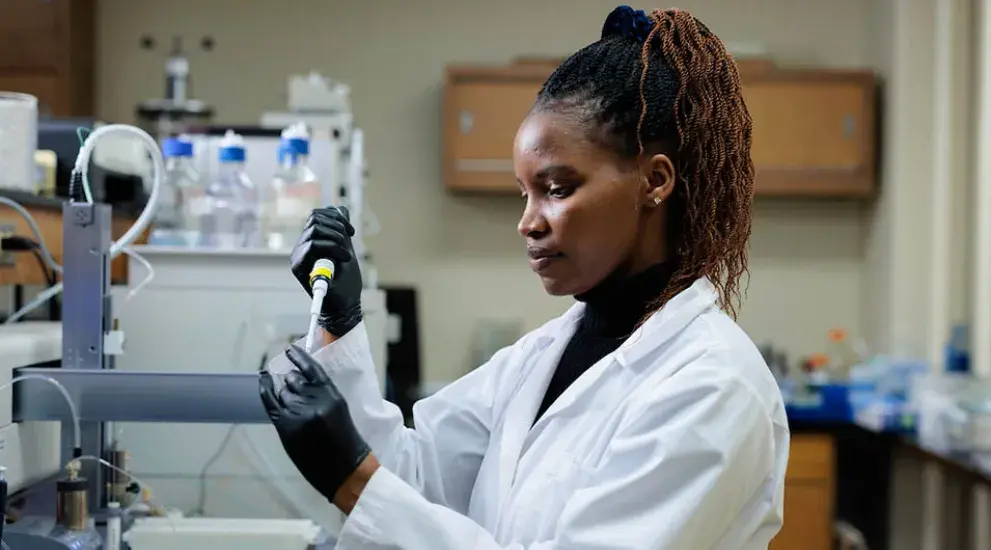 Researcher shown in lab wearing white coat.