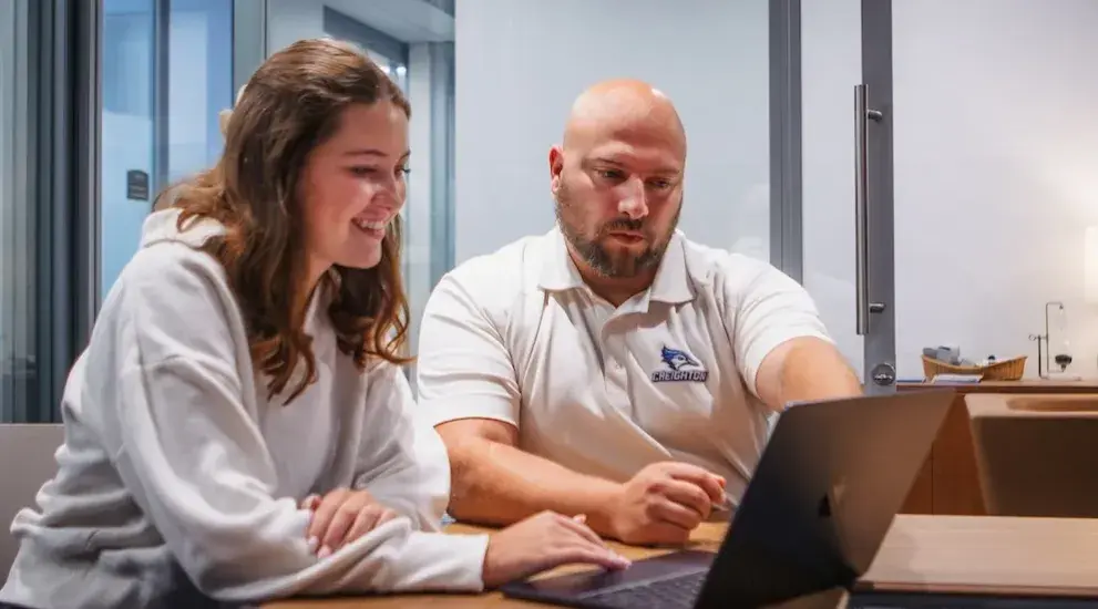 Staff member helping student at laptop.