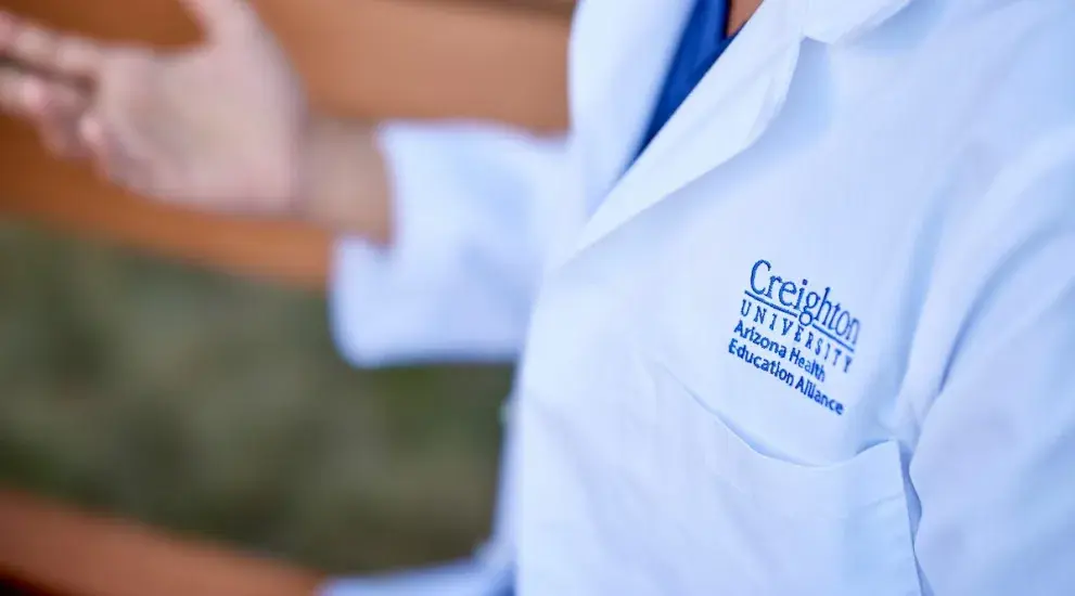 Closeup of white coat with Arizona Health Education Alliance logo on it.